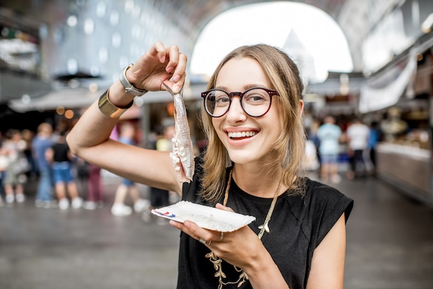 ロッテルダム市場で玉ねぎと伝統的なオランダのおやつとニシンを食べる若い女性