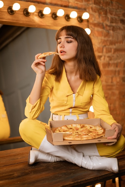 黄色いコンビネに座ってピザを食べる若い女性