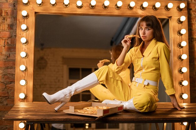 Young woman eating pizza sitting in a yellow kombineh