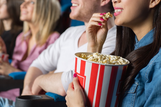 young woman eating popcorn watching movies with her friends at the cinema