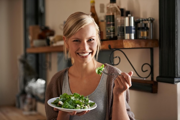 Photo young woman and eating a salad in kitchen with a smile with wellness and lettuce for cooking girl healthy and vegetables on plate for nutrition or diet in house with hungry person in the usa