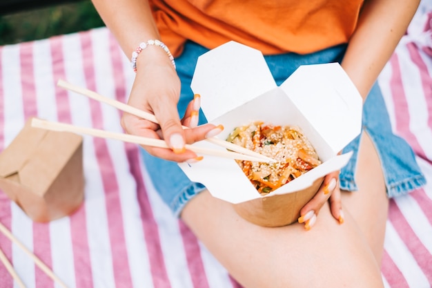 夏の天候を楽しんで、公園で屋外の屋台の食べ物を食べる若い女性。