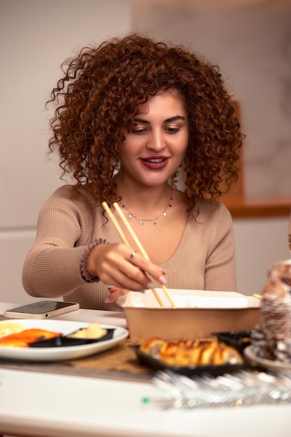 Young woman eating sushi asian food and noodles using choopsticks from take away delivery