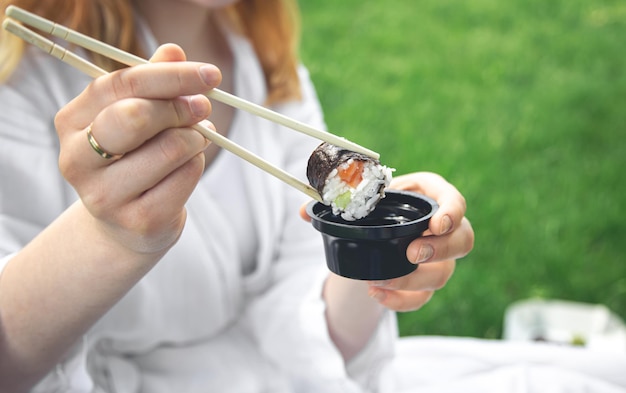 A young woman eating sushi in nature maki roll closeup