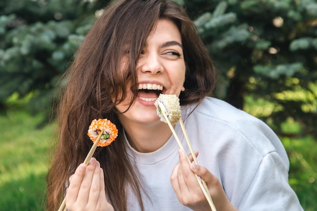 自然の中で公園のピクニックで寿司を食べる若い女性