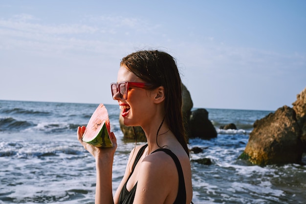 Foto giovane donna che mangia cocomero sulla spiaggia