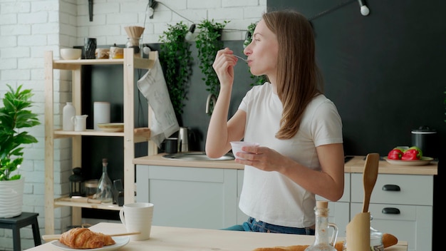 Молодая женщина ест йогурт на кухне дома