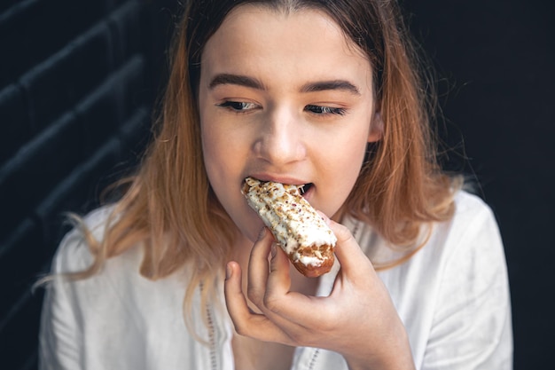 若い女性が食欲をそそるエクレアを食べる