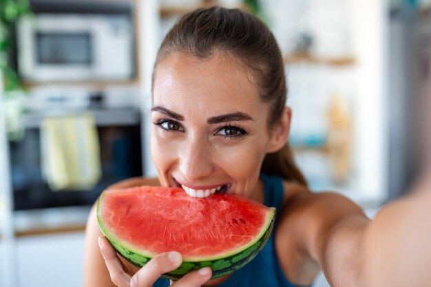 若い女性は台所でスイカのスライスを食べるスイカを楽しんでいる若い女性の肖像画