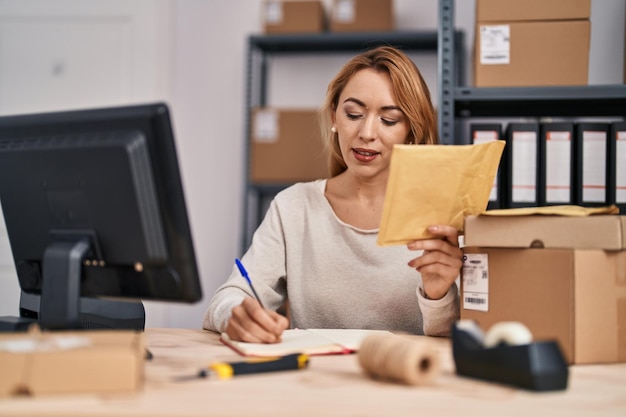 Young woman ecommerce busines worker writing on notebook holding package at office