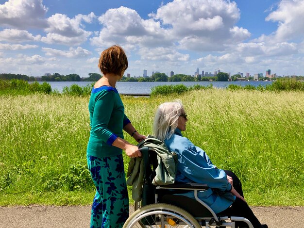 Photo young woman and elderly lady in wheelchair walking along a lake looking at skyline in the distance