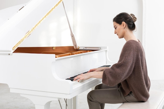 Photo a young woman in elegant casual clothes plays the grand piano on a white background