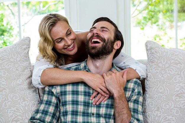 Young woman embracing man from behind against window