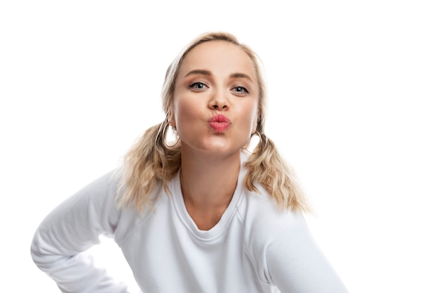 The young woman emotionally folded her lips in a kiss. Pretty blonde with ponytails in a white sweater. White background.