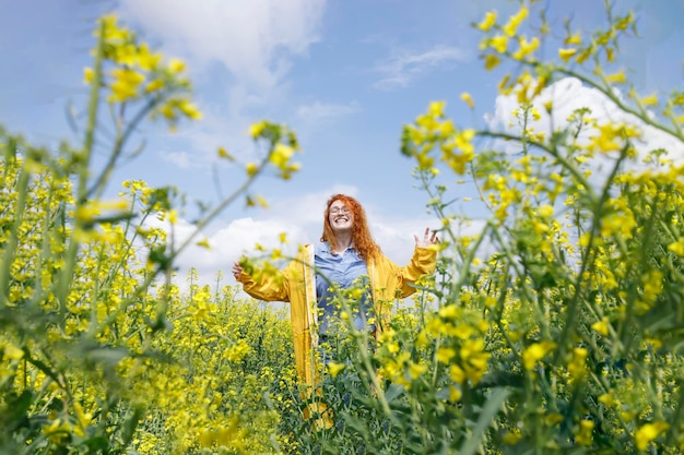 黄色い菜種の畑で雨上がりの美しい夏の日を楽しんでいる若い女性