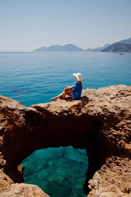 Young woman enjoying holiday on rock with luxury view walking showing emotion on azure sea