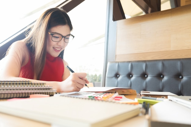 若い女性は、窓の近くに座って読書の本を楽しむコーヒーショップでの窓の反射と彼女の生活の中でリラックス