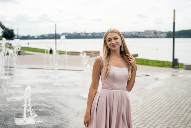 Young woman enjoying summer time posing alone in cute ping dress near lake