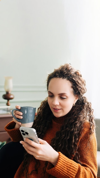 Young woman enjoying a warm drink and online shopping with a smartphone at home happy lady with