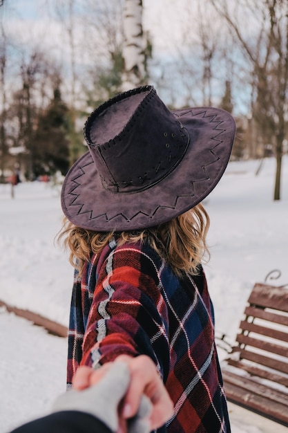 雪の公園で冬の天気を楽しんでいる若い女性。寒波。冬のファッション、休日、休息、旅行のコンセプト。カウボーイハットとポンチョ。巻き毛のブロンドの女の子