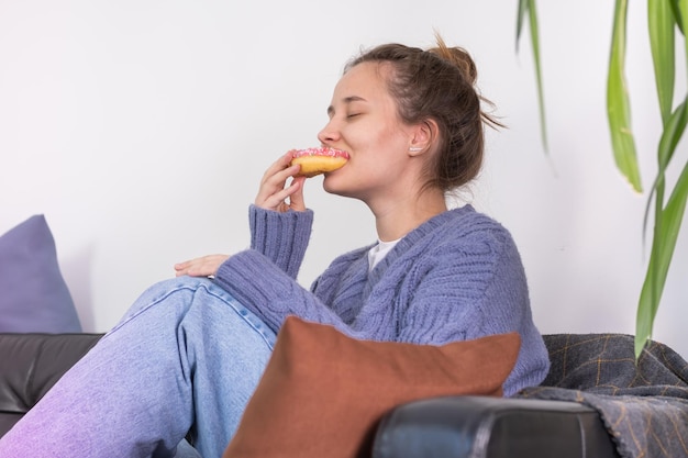 A young woman enjoys eating a delicious mouthwatering donut on the couch