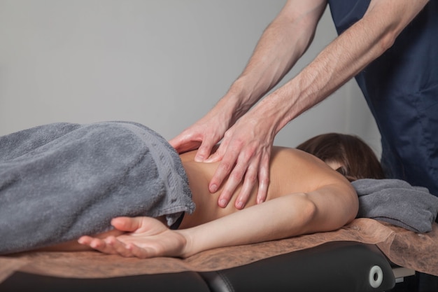 La giovane donna gode del massaggio di benessere sportivo nell'ufficio medico della sala fitness. il massaggiatore domiciliare professionista fa esercizi di massaggio. concetto di relax, bellezza, salute, cura del corpo. copia spazio