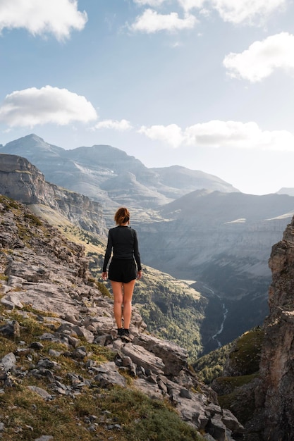 Photo young woman enjoys the views of the ordesa and monte perdido canyon from the heights of a rock during a trekking on a sunny day in the pyrenees