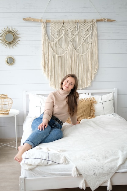 A young woman of European appearance is sitting on the bed in her cozy bedroom with a smile on her face