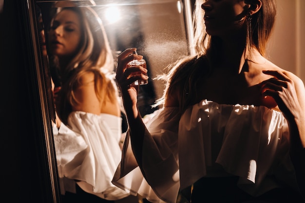 A young woman in an evening dress with perfume stands in front of the home dressing table.The girl uses perfume before going to a party.