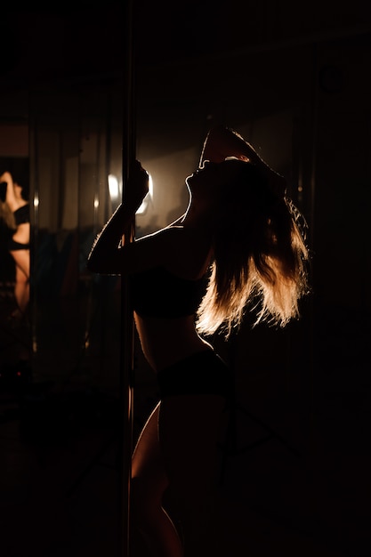 Young woman exercise pole dance on dark.