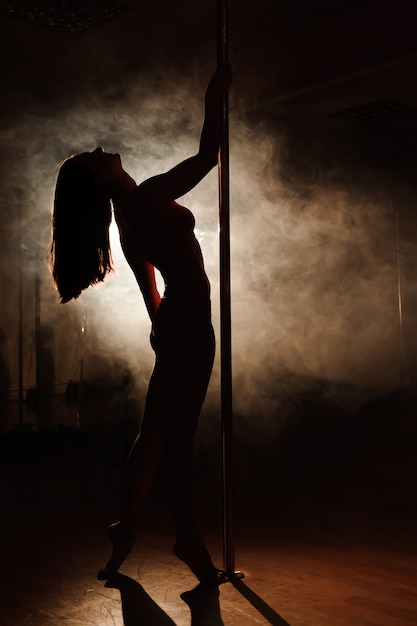 Young woman exercise pole dance on dark.