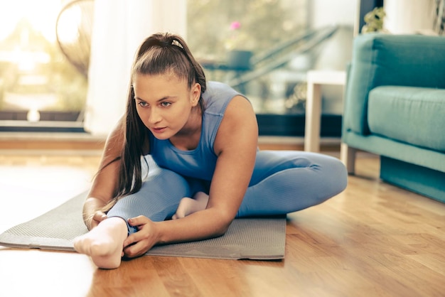 Young woman exercising at home in the morning. She is doing stretching workout on exercise mat.