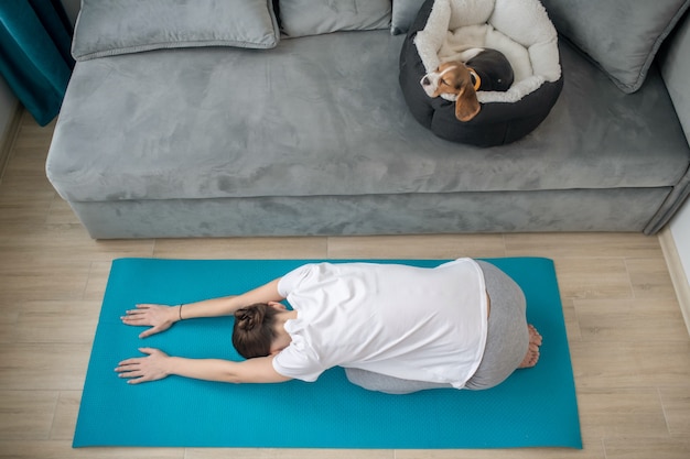 A young woman exercising at home while her puppy sleeping in a dogs place