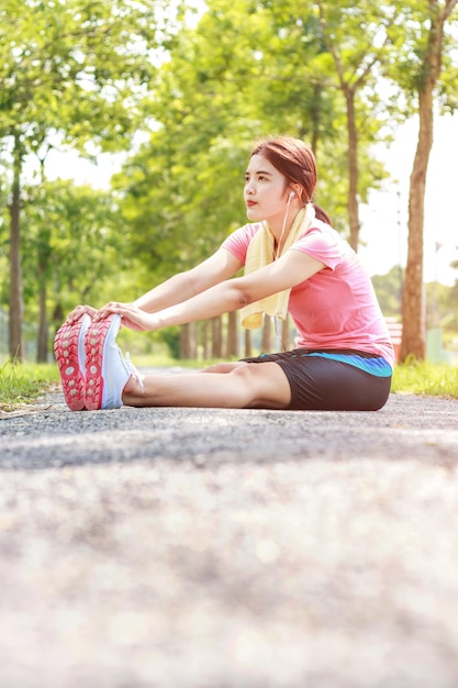 Young woman exercising while sitting on footpath at park