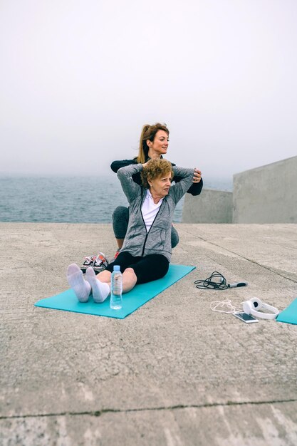 Young woman exercising with senior woman by sea pier