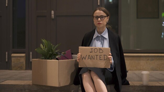 Young woman in eyeglasses in office clothes with sign job\
wanted