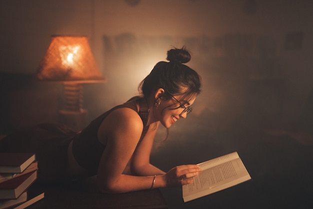 Photo young woman in eyeglasses reading a book in a cozy living room