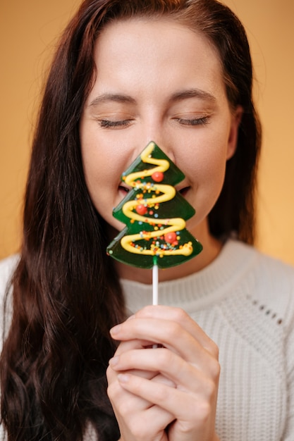 若い女性は、新年のクリスマスの伝統的な休日の甘いモミロリポップでクローズアップに直面します