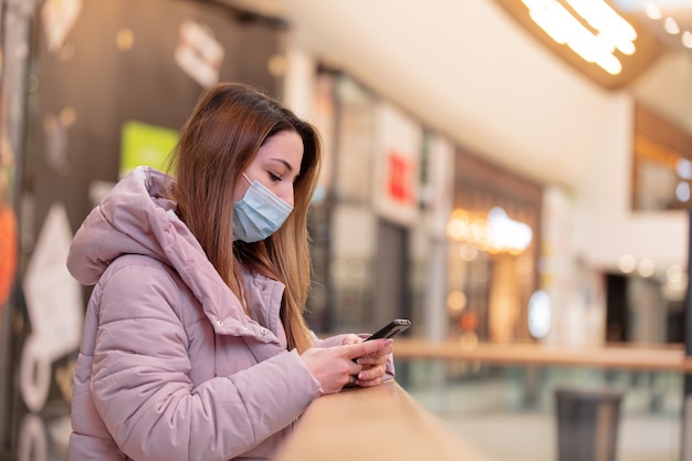 Young woman in face mask using mobile phone in city mall