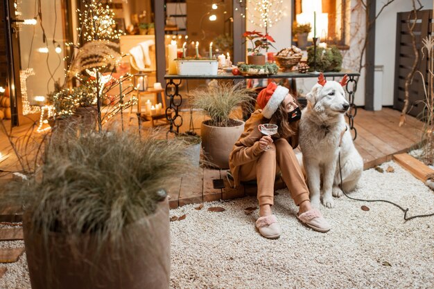 Photo young woman in facial mask celebrating with a dog new year holidays at home. concept of quarantine and self-isolation during the epidemic on holidays