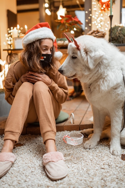 自宅で犬と一緒に年末年始を祝うフェイシャルマスクの若い女性。休日の流行中の検疫と自己隔離の概念