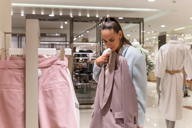 A young woman in a fashion boutique chooses clothes Beautiful stylish brunette in a blue jacket Fashion Style