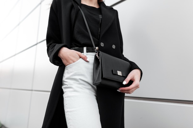 Young woman in a fashionable black coat in vintage white jeans with handbag