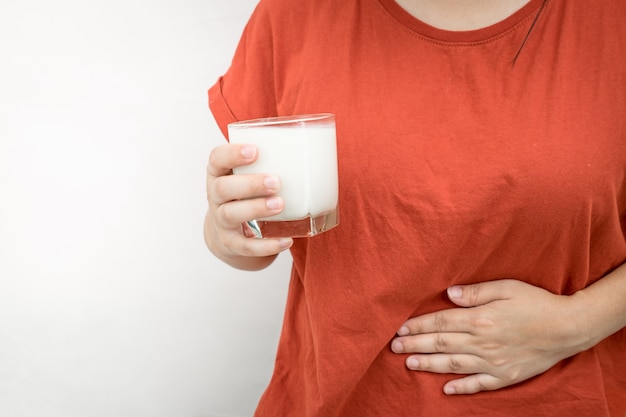 La giovane donna sente mal di stomaco dopo aver bevuto del latte. mano che tiene il bicchiere di latte su bianco.