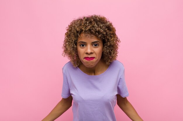 Young   woman feeling clueless and confused, having no idea, absolutely puzzled with a dumb or foolish look against pink wall