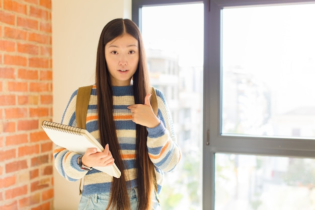 Young woman feeling confused, puzzled and insecure, pointing to self wondering