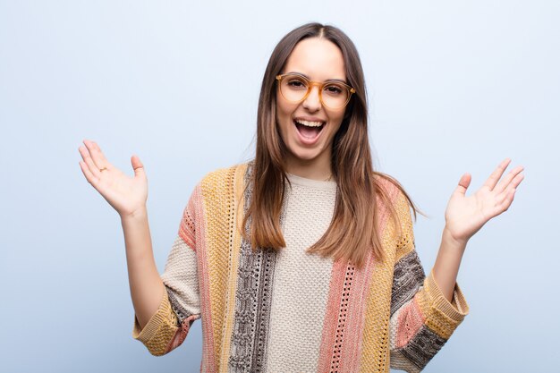 Young woman feeling happy, excited, surprised or shocked, smiling and astonished at something unbelievable on blue wall