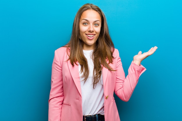 Giovane donna felice, sorpresa e allegra, sorridente con atteggiamento positivo, realizzazione di una soluzione o idea contro il muro blu