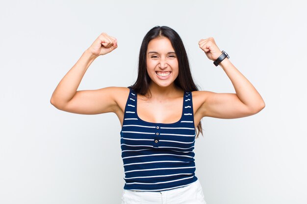 Young woman feeling happy, surprised and proud, shouting and celebrating success with a big smile