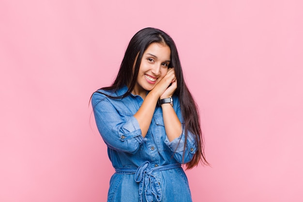 Young woman feeling in love and looking cute, adorable and happy, smiling romantically with hands next to face